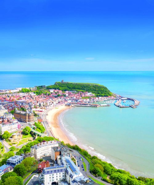 Aerial photo of the town centre of Scarborough in East Yorkshire in the UK showing the coastal beach and harbour with boats and the Scarborough Castle on a bright sunny summers day